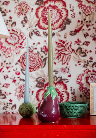 A glossy purple ceramic vase shaped like an eggplant with green leafy accents shown with the mayfair tray hold all rattan basket in green