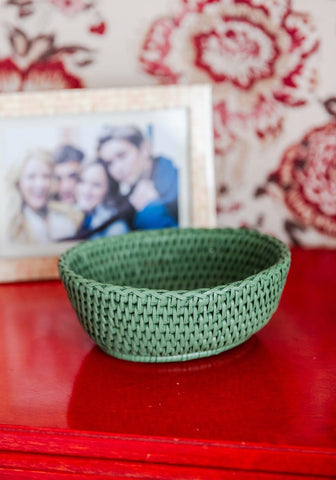 A woven green rattan basket with a tight knit pattern sits on a red surface in the mayfair tray hold all style
