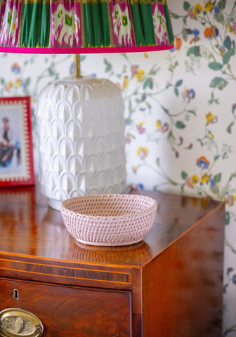 A delicate pink mayfair trinket hold all basket made of woven rattan with a textured pattern on a wooden surface