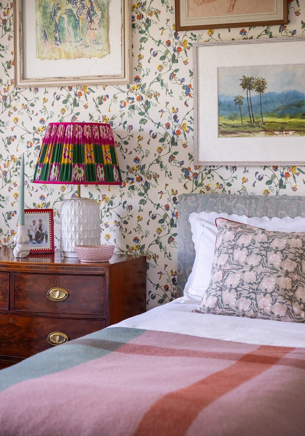 A vibrant patterned lampshade with pink green and yellow stripes on a white ceramic base next to a pink rattan basket