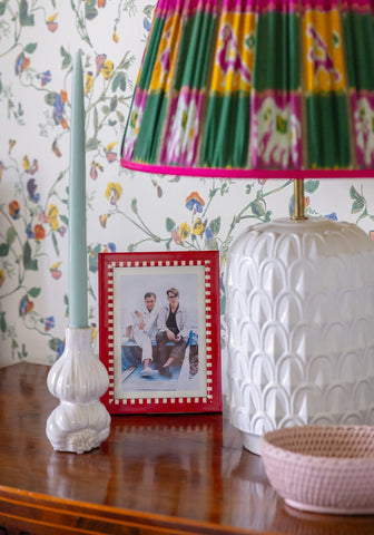 White ceramic table lamp with pleated colorful ikat shade next to a pink mayfair trinket hold all rattan basket