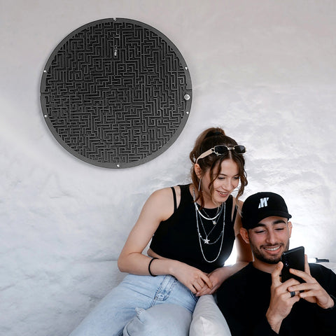 Black circular maze board wall game with metallic finish featuring target area and ball holder for fun play
