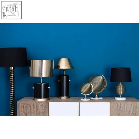 The melora round marble gold finish table lamp base with marble gold finish on a wooden console against blue wall