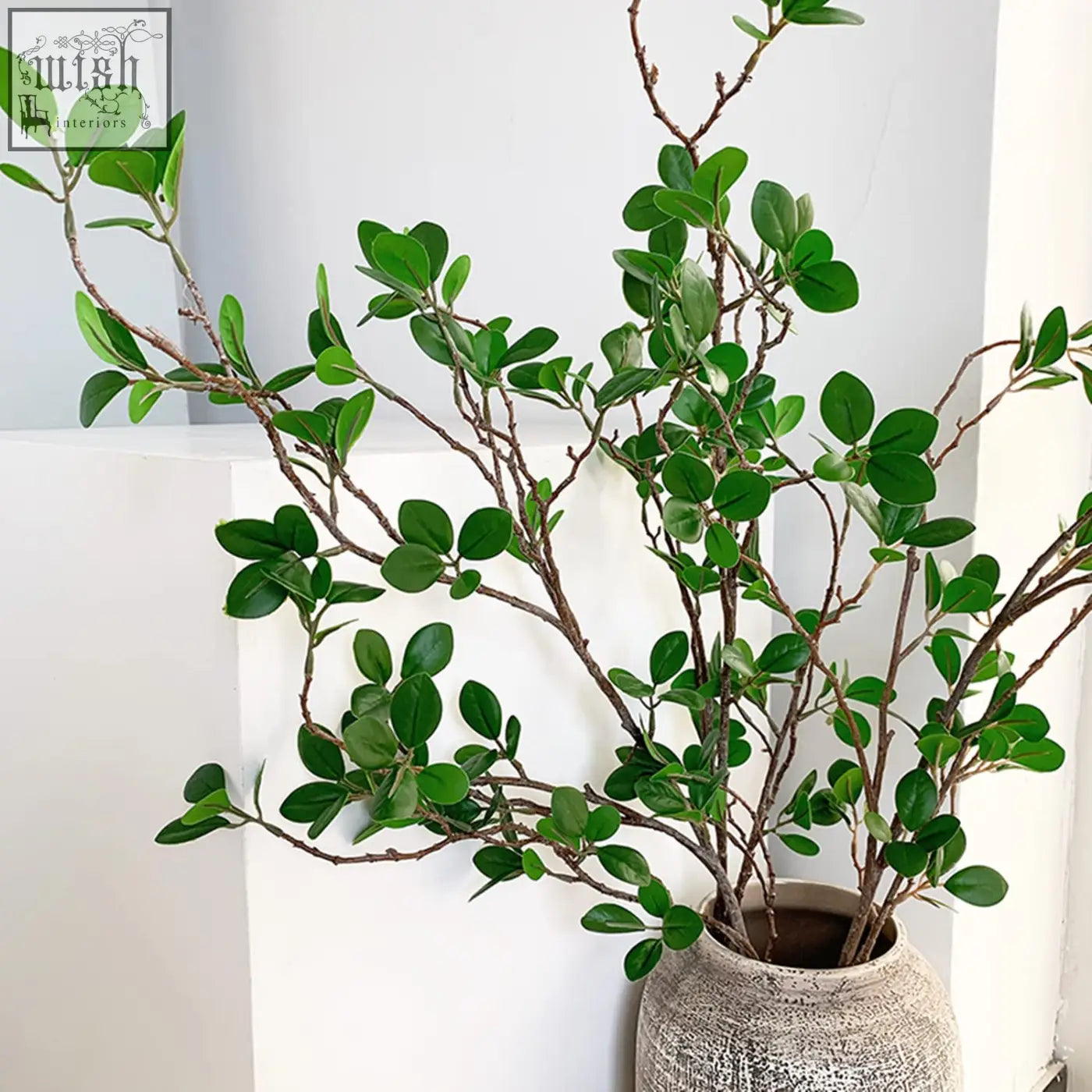 A textured light gray ceramic vase with lush green faux branches of artificial plants for home decor