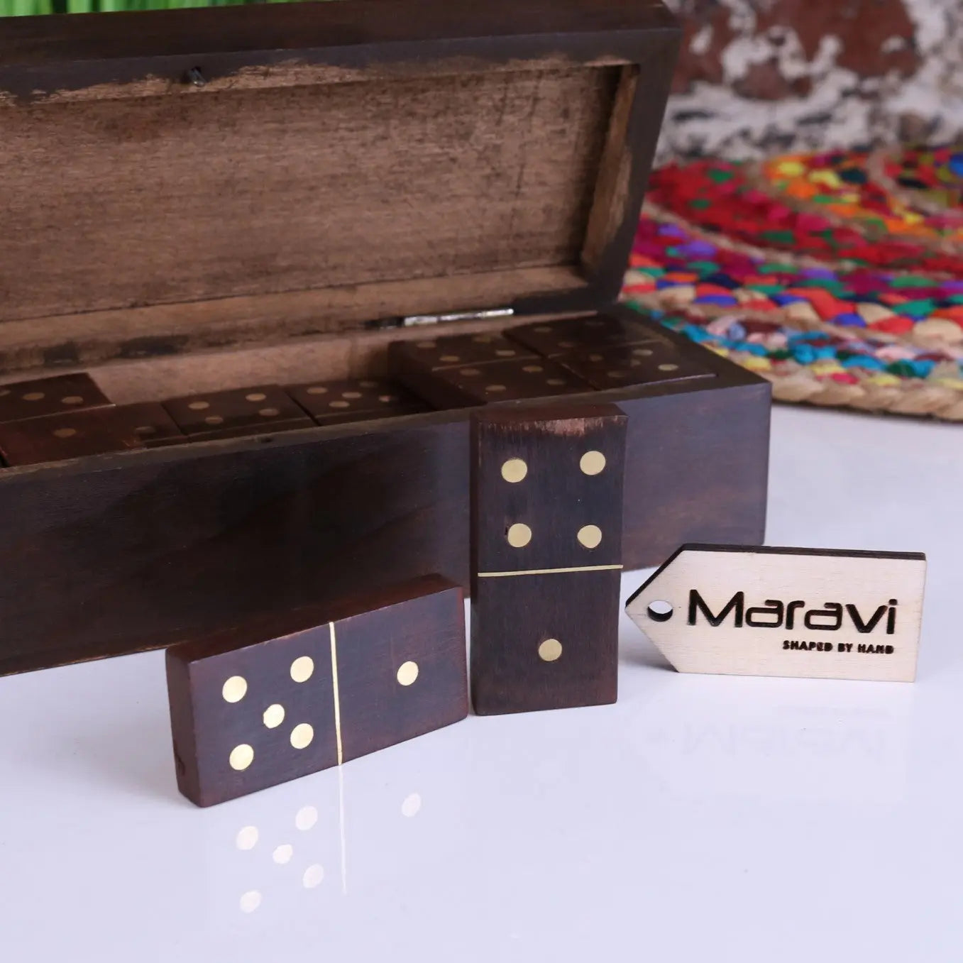 Dark wooden domino set with gold dots neatly arranged beside a mera wooden domino carved storage box and tag
