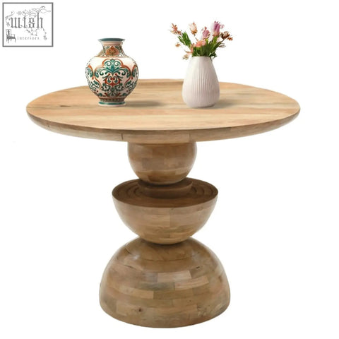 Light-colored mango wood dining table with round top and sculptural stepped base perfect for any space