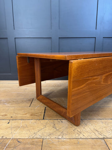 A warm polished teak drop leaf coffee table with clean lines featuring a minimalist mid century design