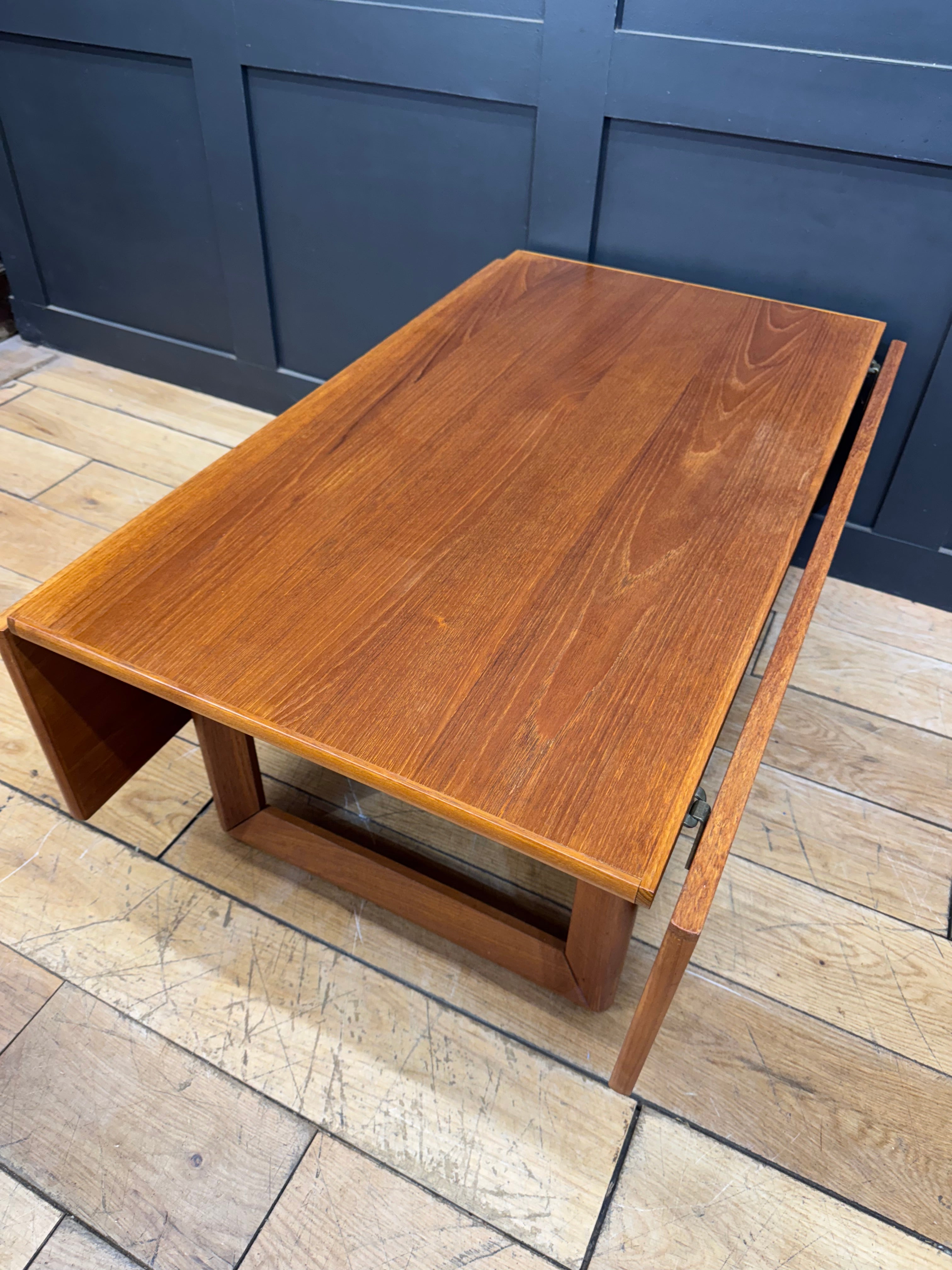 A sleek teak mid century modern coffee table with warm amber finish featuring a functional drop leaf design