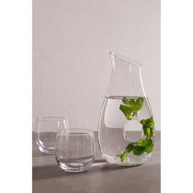 Clear glass carafe with curved spout and circular handle filled with mint leaves paired with mila set glass tumblers with wide bowl