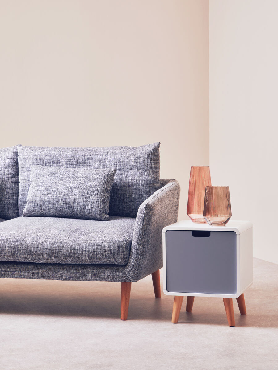 Gray textured fabric sofa with natural legs and matching pillows next to a light two-tone milo 1 door cabinet