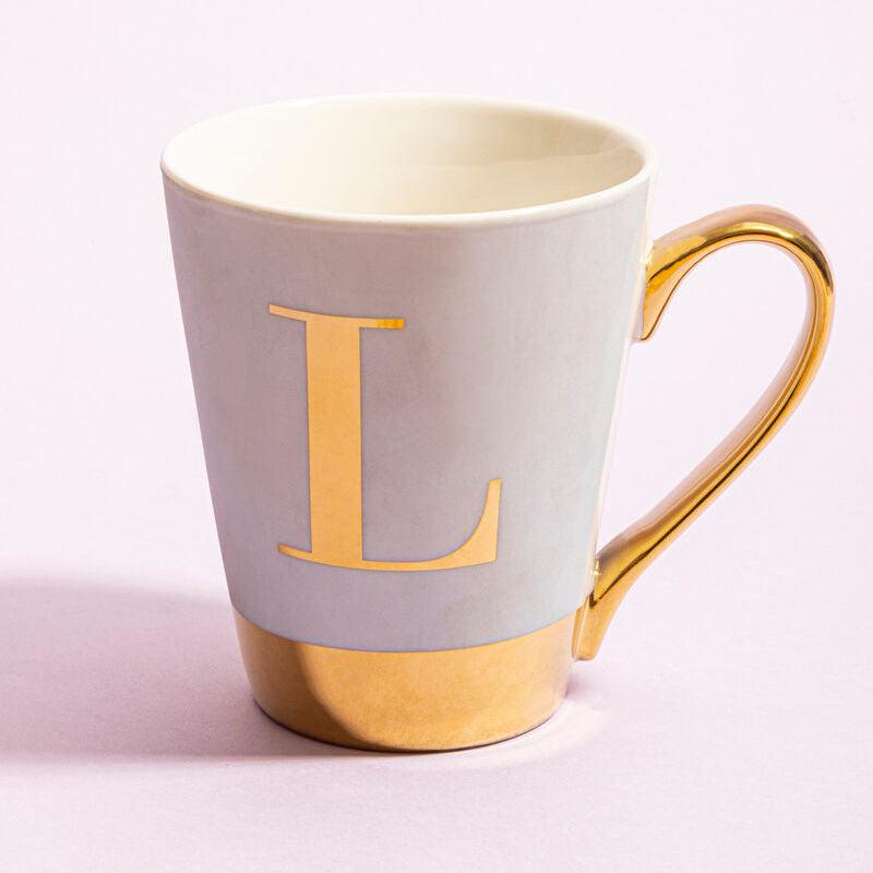 A sleek light gray ceramic mug with gold handle and base featuring a bold gold l in green frosted deco style