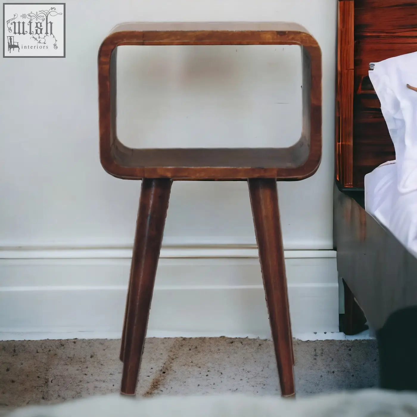 A sleek mini chestnut curved open bedside table made of wood with an open shelf and tapered legs