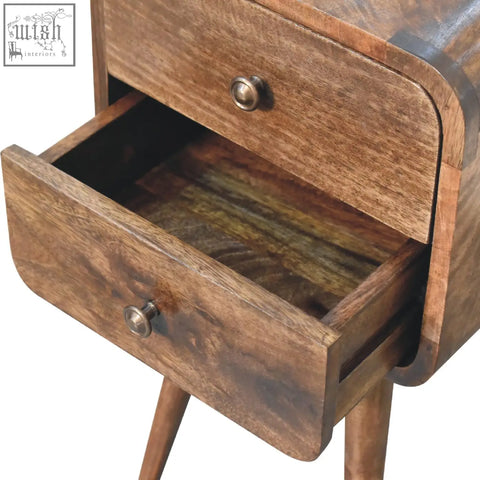 A mini curved grey washed bedside table made of solid mango wood with two curved drawers and round brass knobs
