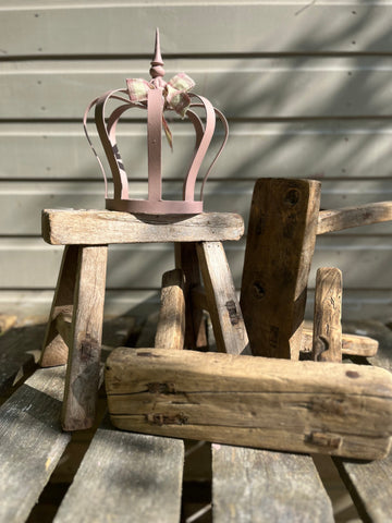 A delicate pink metal crown with a small bow resting on a rustic wooden mini elm stool