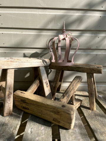 A delicate pink metal crown with a small bow resting on rustic wooden mini elm stools