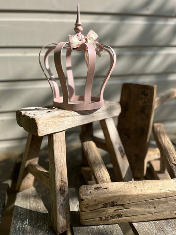 A delicate pink metal crown ornament with a small bow resting on a rustic wooden mini elm stool