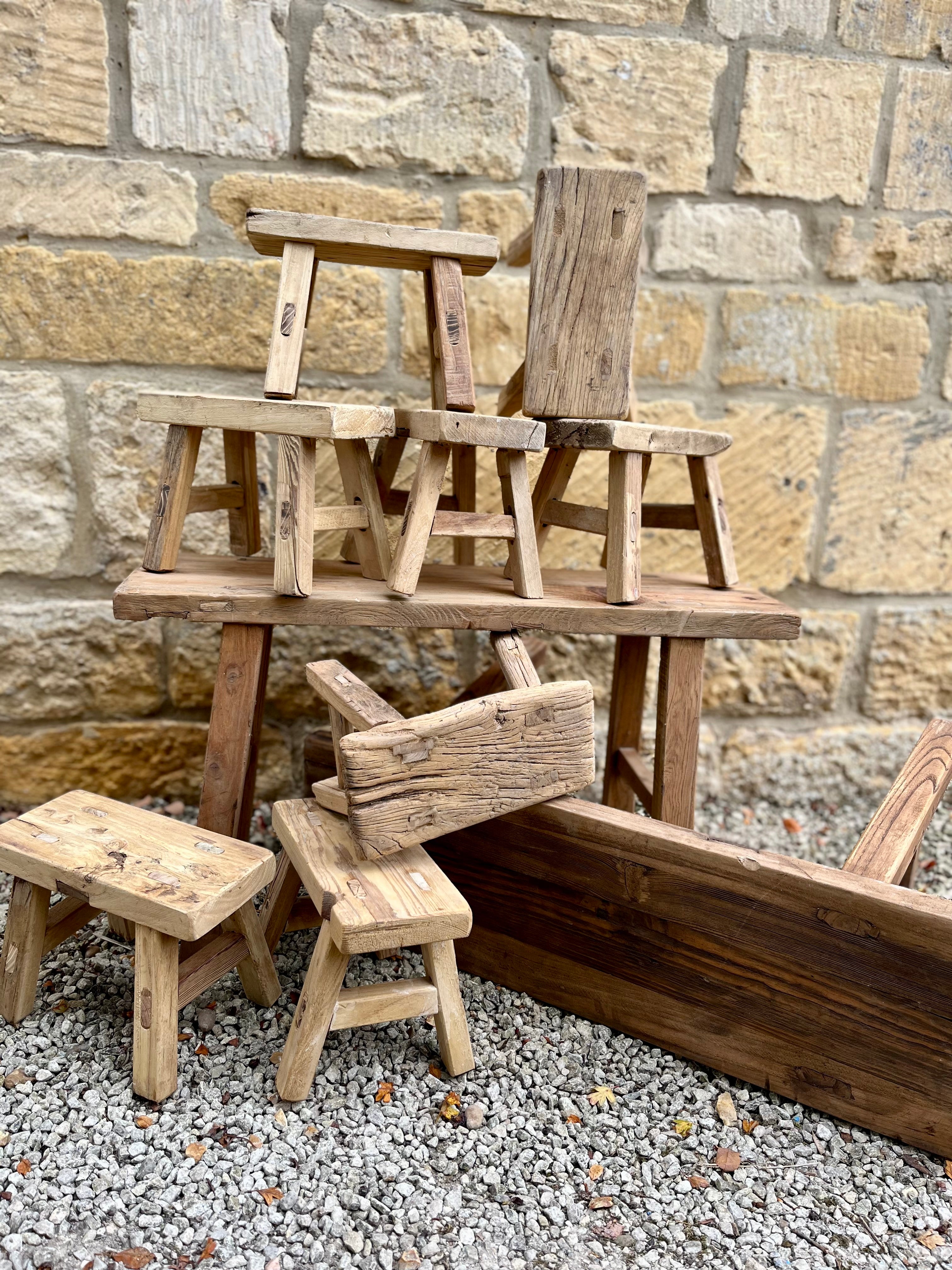 Rustic mini elm stools with natural wood grain and weathered finish stacked casually against stone wall