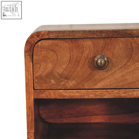 A warm honey caramel mango wood mini bedside with open slot and curved top featuring a brass knob drawer