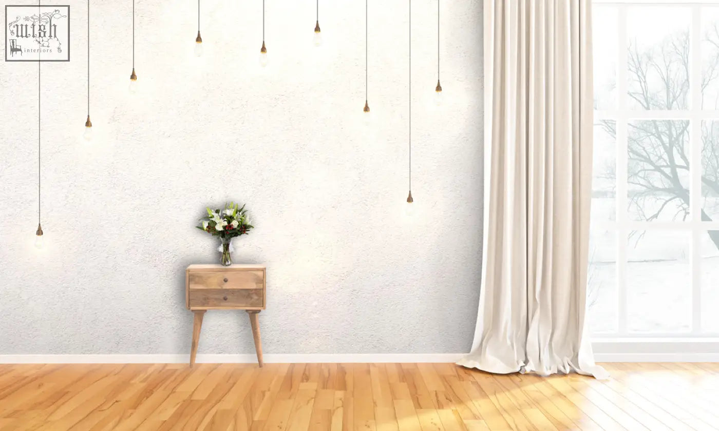 A delicate white and green flower bouquet sits on a modern solid wood bedside table in light wood finish