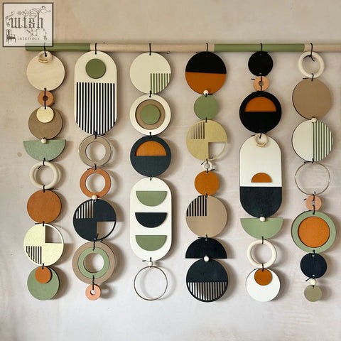 A modern wall art piece featuring layered wooden discs and rings in beige olive green black orange and white tones