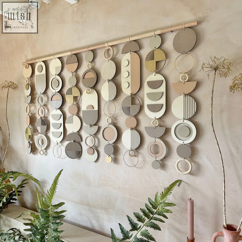 A modern wall art featuring layered wooden and painted circular shapes in beige gray and soft pastel pink tones