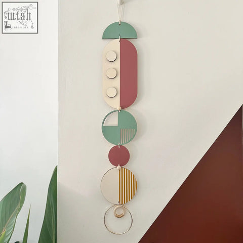 A modern wall art piece featuring layered wooden geometric shapes in muted green terracotta cream and gold with stripes