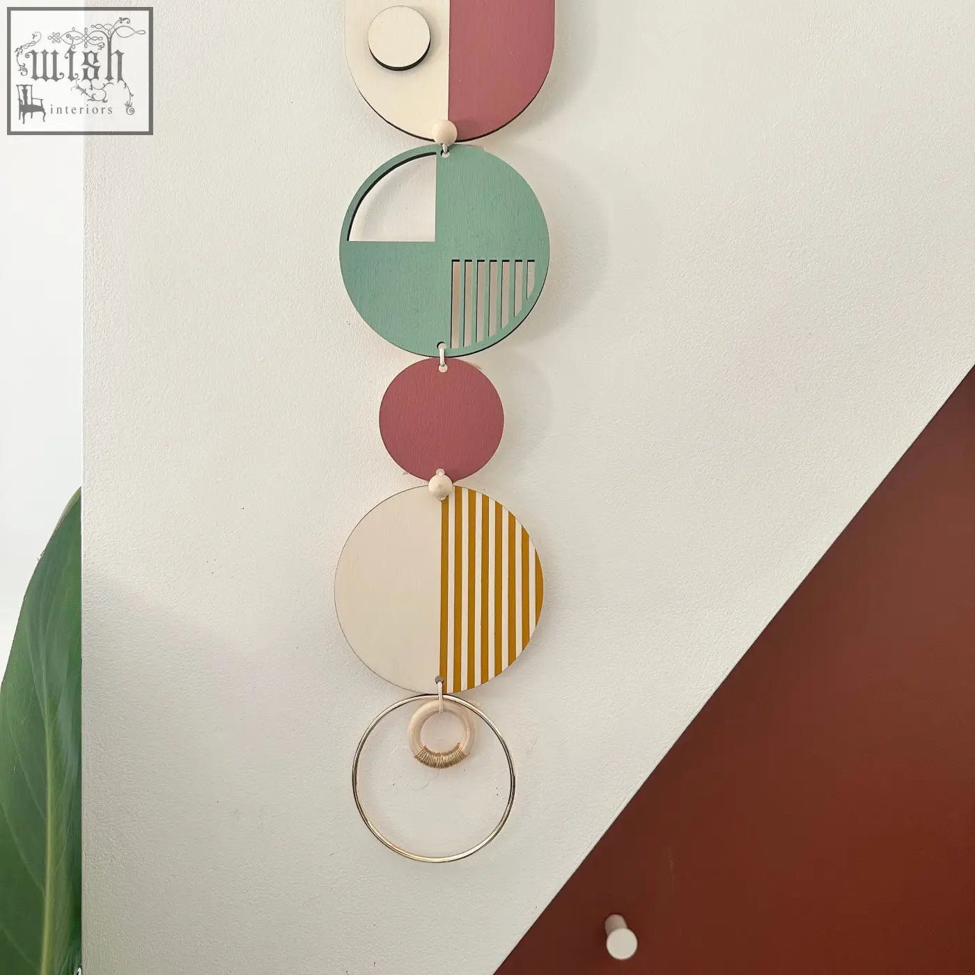 A modern wall art piece featuring five circular wooden discs in pastel and terracotta tones with geometric patterns
