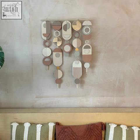 A modern wall art piece with layered wooden shapes, gold metal hoop detailing, and blush pink accents in soft tones