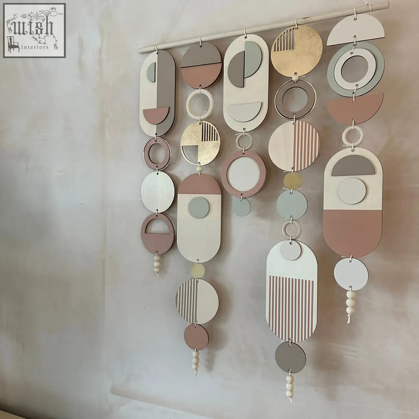 A modern wall art piece with a gold metal hoop and layered wooden shapes in blush pink accents and muted tones
