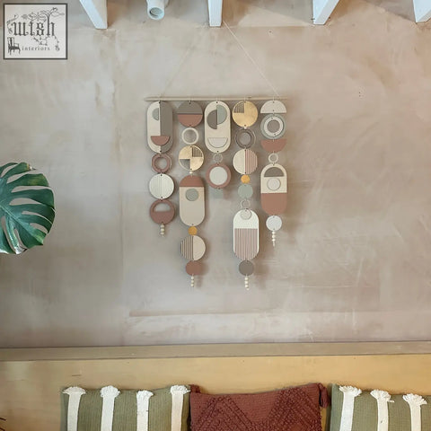 Modern wall art featuring layered wooden shapes in earthy tones with gold metal hoop detailing and pink accents