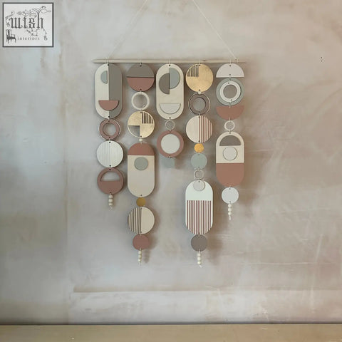 Modern wall art with gold metal hoop detailing featuring layered wooden and painted metal pieces with pink accents