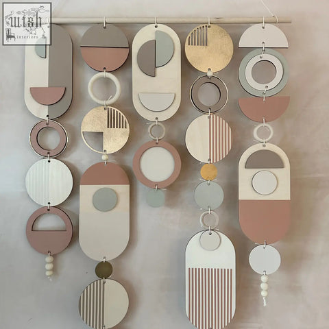 Modern wall art with gold metal hoop detailing featuring layered wooden shapes in soft pastel tones and pink accents