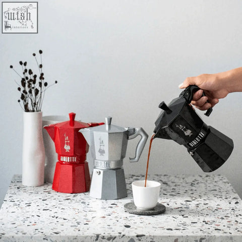 Black bialetti moka express exclusive with glossy finish pouring coffee into white cup for perfect brew