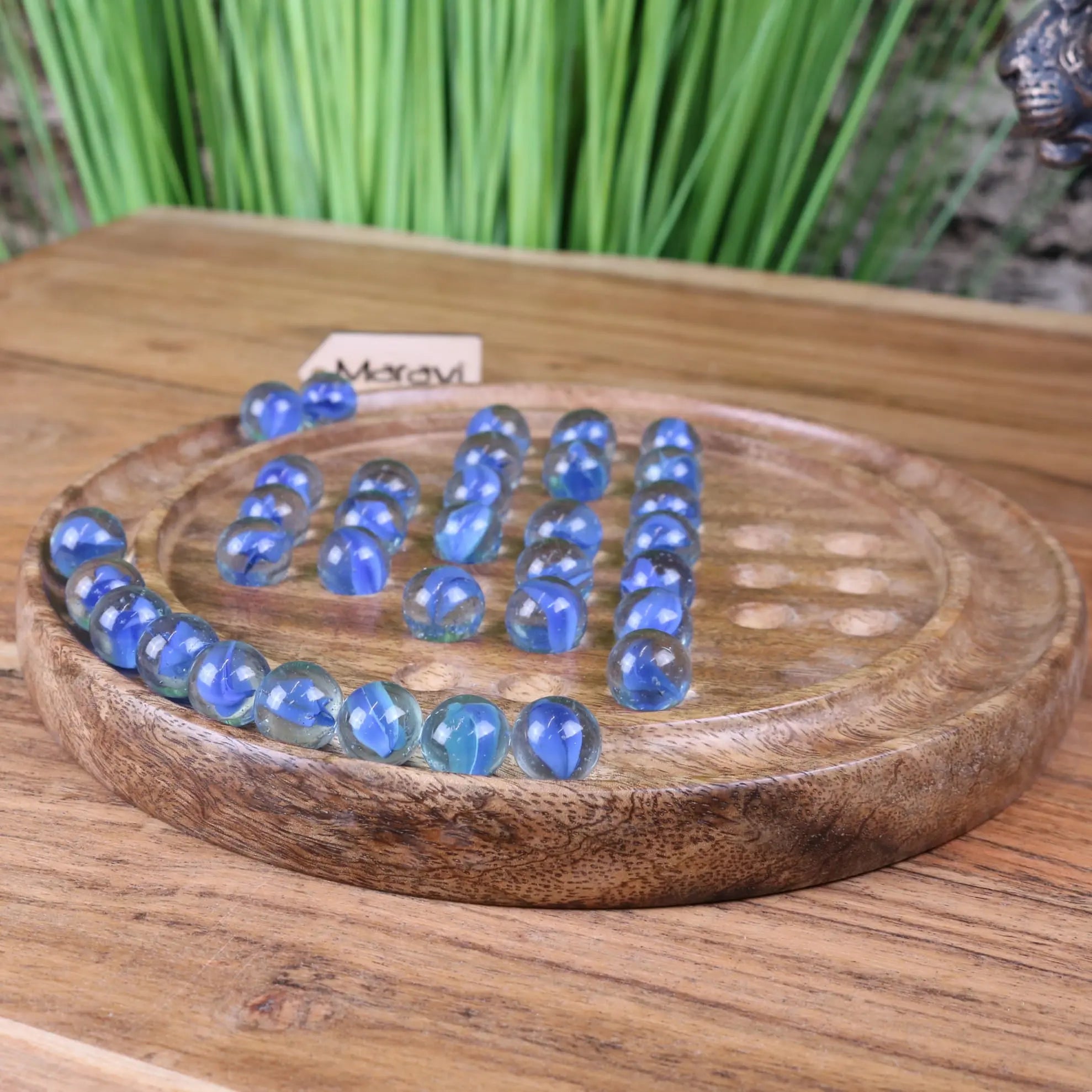 Moksha deluxe wooden solitaire board game set with blue glass marbles on a natural wood solitaire board surface