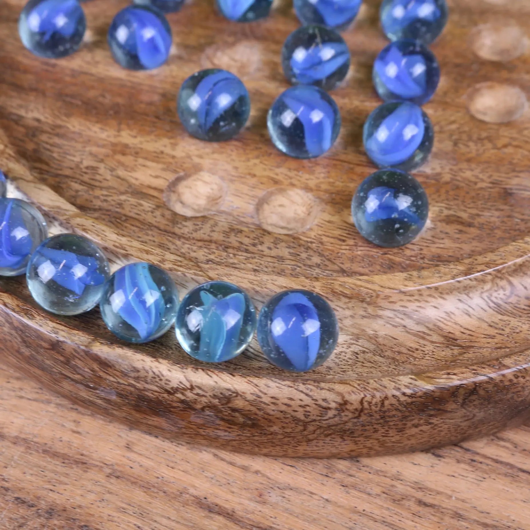 Blue marbles with swirling patterns on a wooden surface in the moksha deluxe solitaire board game set