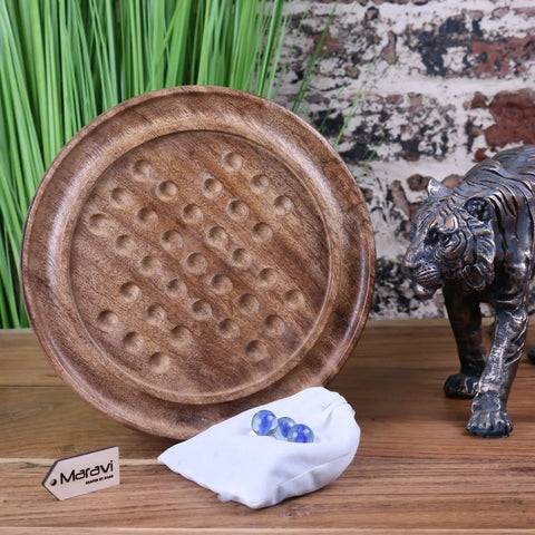 Moksha deluxe wooden solitaire board game with brown circular indentations and blue glass marbles on white cloth