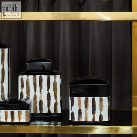 Set of four modern ceramic mona brushstroke trinket boxes with black lids and brown brushstroke patterns on a gold shelf