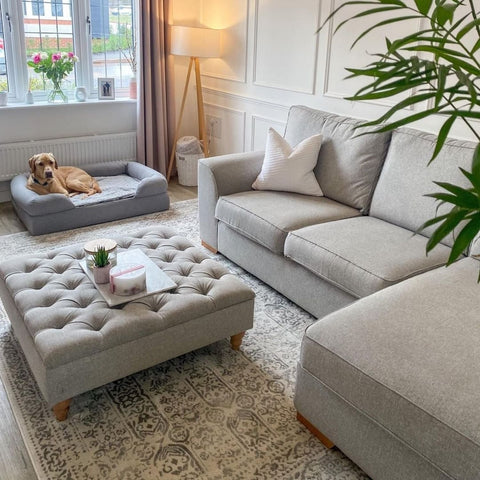 Gray tufted ottoman with wooden legs on soft cream rug showcasing the montana cream rug texture and color