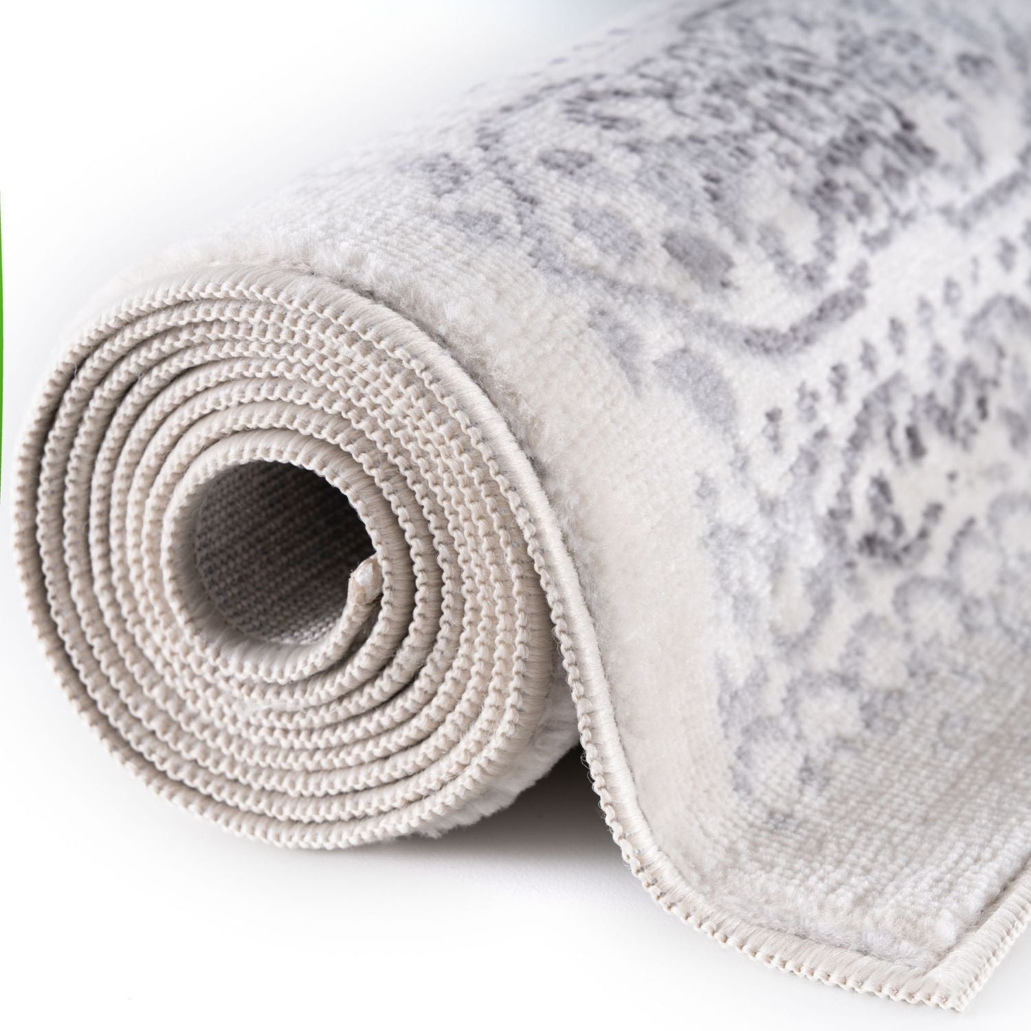 A montana cream rug rolled up with a subtle gray ornate pattern and textured looped pile in beige cream tones