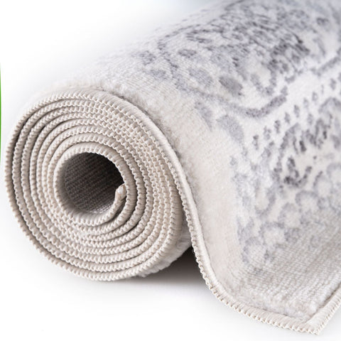 A montana cream rug rolled up with a subtle gray ornate pattern and textured looped pile in beige cream tones
