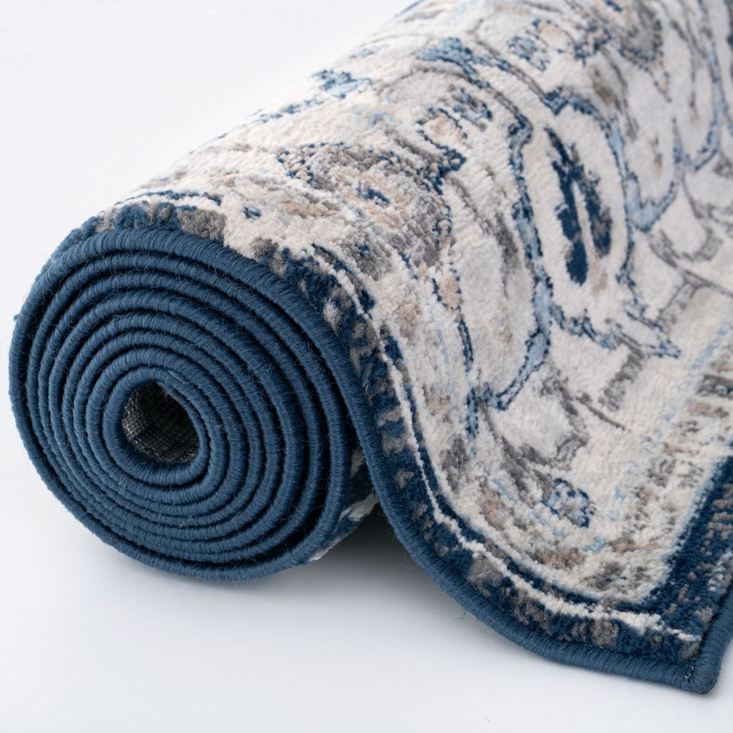 A rolled-up montana vintage navy area rug with plush texture vintage-inspired blue beige and gray pattern and solid border