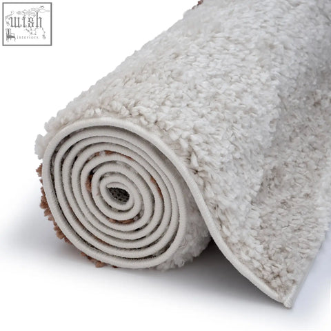 A plush moodi shaggy cream rug rolled neatly showing its soft off-white shaggy texture on a white surface