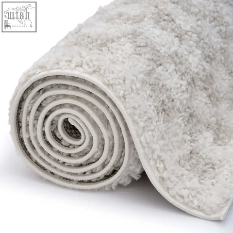 A plush moodi shaggy light beige nomari rug rolled into a tight spiral showcasing its soft shaggy texture