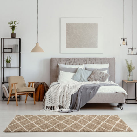 Gray upholstered bed with tufted headboard on a moroccan beige shaggy rug layered with white and gray bedding fabrics