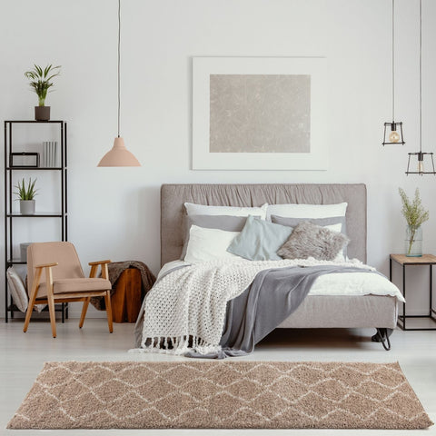 Moroccan beige shaggy rug with geometric diamond pattern in beige shaggy texture lies in front of a bed