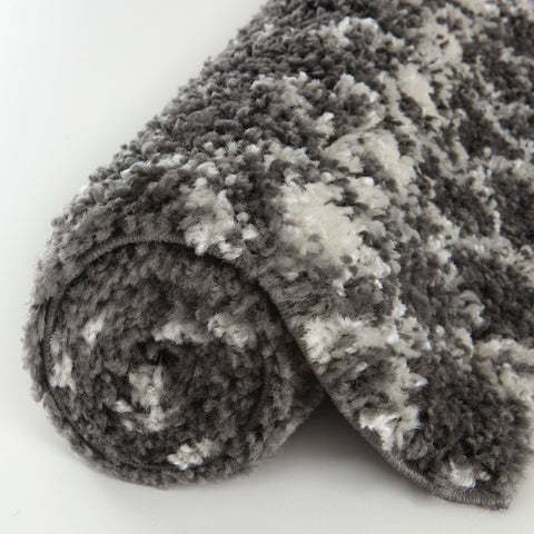 A plush moroccan dark grey shaggy rug rolled up showing its soft textured surface and grey shaggy material