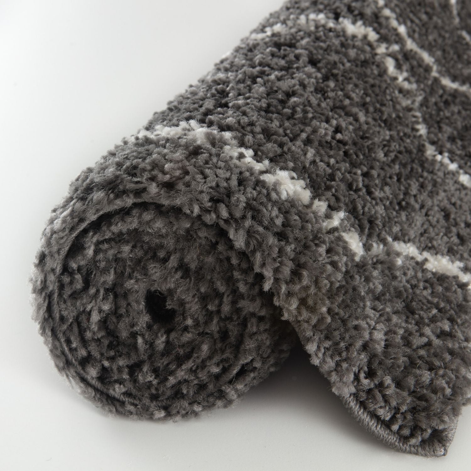 A plush moroccan dark grey shaggy rug rolled up with soft gray and white striped texture for cozy spaces