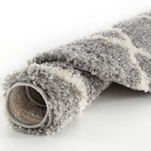 A plush rolled-up moroccan grey shaggy rug with a soft grey and white geometric pattern and shaggy texture