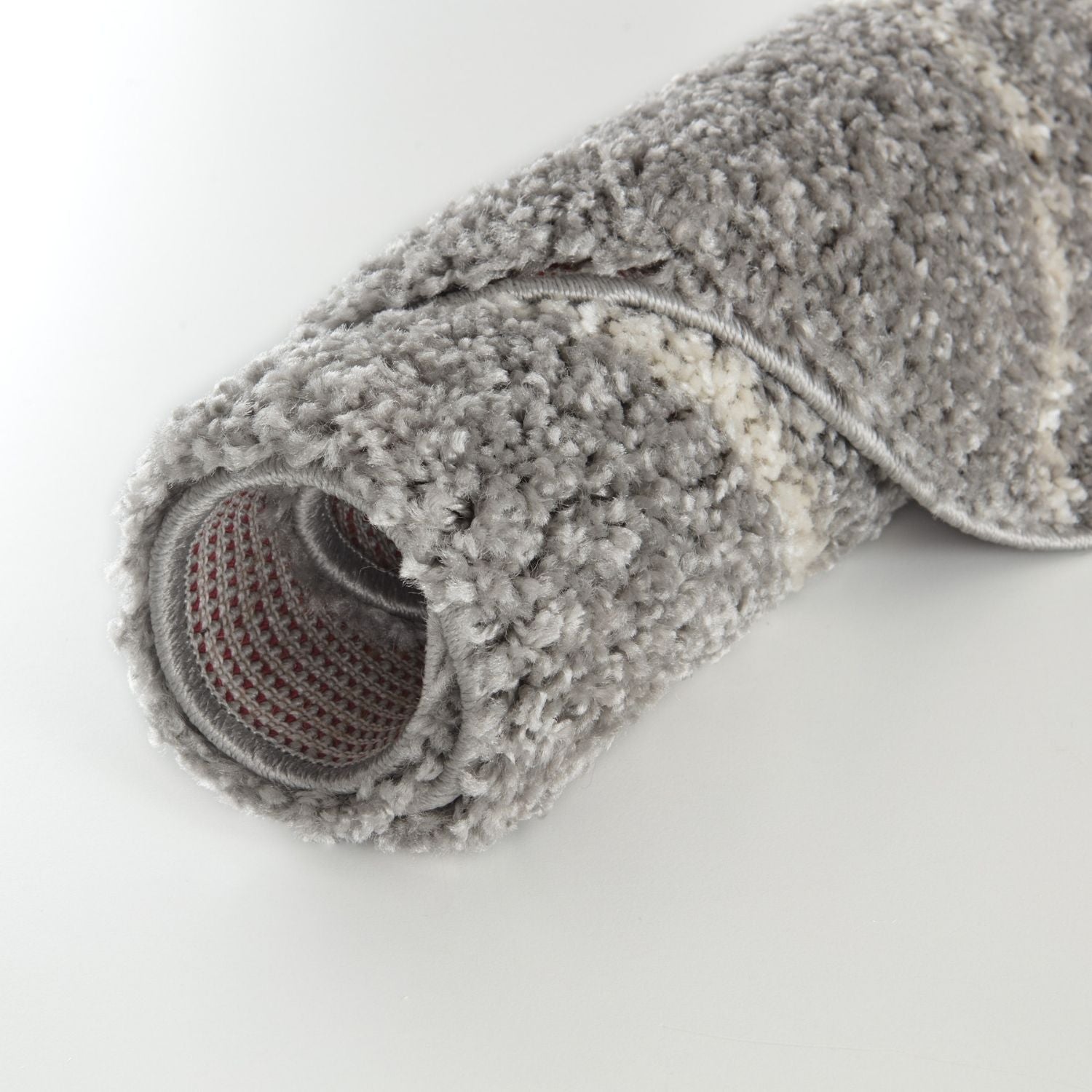 A roll of plush moroccan grey shaggy rug with textured surface and visible woven backing showing the back side