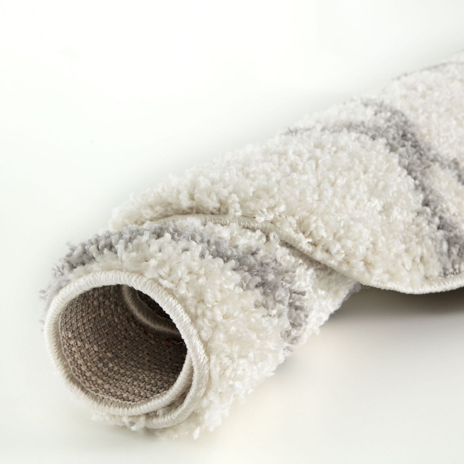 A plush rolled-up moroccan ivory shaggy rug in soft white and gray with subtle striped patterns